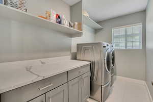 Laundry area featuring light tile patterned flooring, washing machine and clothes dryer, and cabinet space