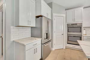 Kitchen featuring tasteful backsplash, stainless steel appliances, white cabinets, and light wood finished floors