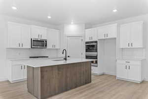 Kitchen with stainless steel appliances, a kitchen island with sink, light stone countertops, light wood-type flooring, and recessed lighting