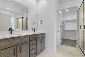 Full bath with double vanity, a walk in closet, a shower stall, and recessed lighting