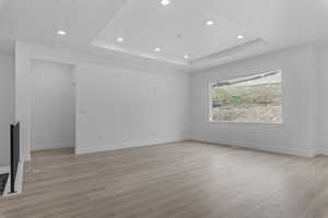 Spare room featuring recessed lighting, light wood-style flooring, and a raised ceiling