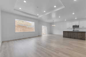 Unfurnished living room with light wood-style floors, a textured ceiling, hanging lights, and a tray ceiling