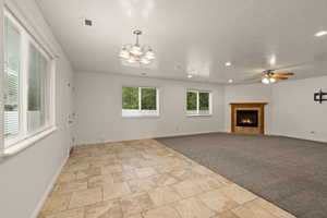 Unfurnished living room featuring light colored carpet, a fireplace, hanging lights, a textured ceiling, and ceiling fan