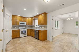 Kitchen with light countertops, wood finish cabinets, white appliances, decorative backsplash, and suspended lighting