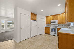 Kitchen with light countertops, white appliances, light tile patterned floors, decorative backsplash, and a textured ceiling