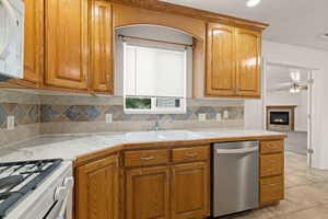 Kitchen featuring light countertops, white appliances, a glass covered fireplace, wood finish cabinetry, and a ceiling fan