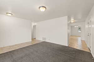 Empty room featuring a textured ceiling, light tile patterned floors, and light colored carpet