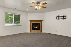 Unfurnished living room with carpet, a tile fireplace, a ceiling fan, and a textured ceiling