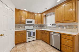 Kitchen featuring light countertops, white appliances, wood finish cabinetry, and recessed lighting
