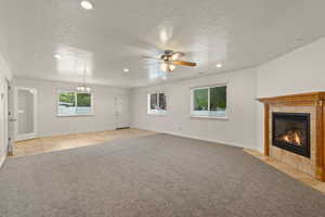 Unfurnished living room with light colored carpet, ceiling fan, a fireplace, hanging lights, and a textured ceiling
