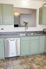 Kitchen with green cabinets, stainless steel dishwasher, and light stone finish flooring