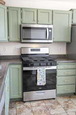 Kitchen featuring green cabinets, stainless steel appliances, dark countertops, and light stone finish flooring