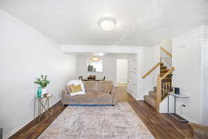 Living room featuring dark wood-style floors, a textured ceiling, and ornamental molding