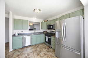 Kitchen featuring stainless steel appliances, green cabinetry, a textured ceiling, and dark countertops