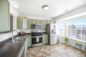 Kitchen with green cabinetry, stainless steel appliances, dark countertops, and a textured ceiling
