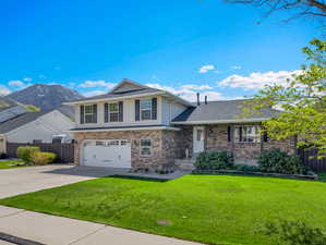 Split level home featuring an attached garage, concrete driveway, brick siding, a mountain view, and a shingled roof
