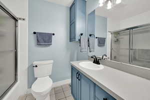 Full bath with vanity, light tile patterned floors, and bath / shower combo with glass door