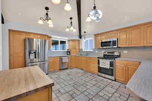 Kitchen featuring stainless steel appliances, butcher block countertops, hanging light fixtures, tasteful backsplash, and lofted ceiling with beams