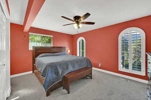 Carpeted bedroom with a closet, a ceiling fan, and beamed ceiling
