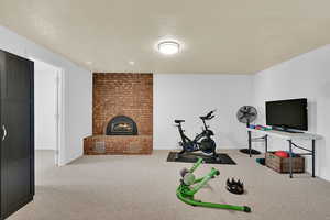 Exercise room featuring a textured ceiling, light carpet, and a fireplace