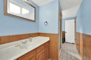 Full bath with a shower stall, vanity, wooden walls, wainscoting, and light tile patterned floors