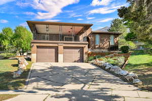 View of front of home featuring a balcony, brick siding, driveway, and an attached garage