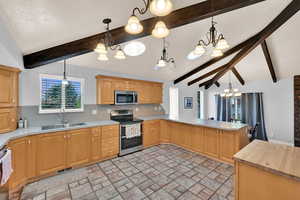 Kitchen featuring hanging lights, stainless steel appliances, a peninsula, plenty of natural light, and lofted ceiling with beams