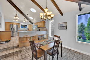 Dining area featuring vaulted ceiling with beams, suspended lighting, and stone tile flooring