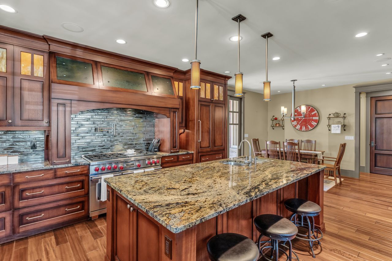 Kitchen with backsplash, range with two ovens, light stone counters, a breakfast bar area, and glass insert cabinets