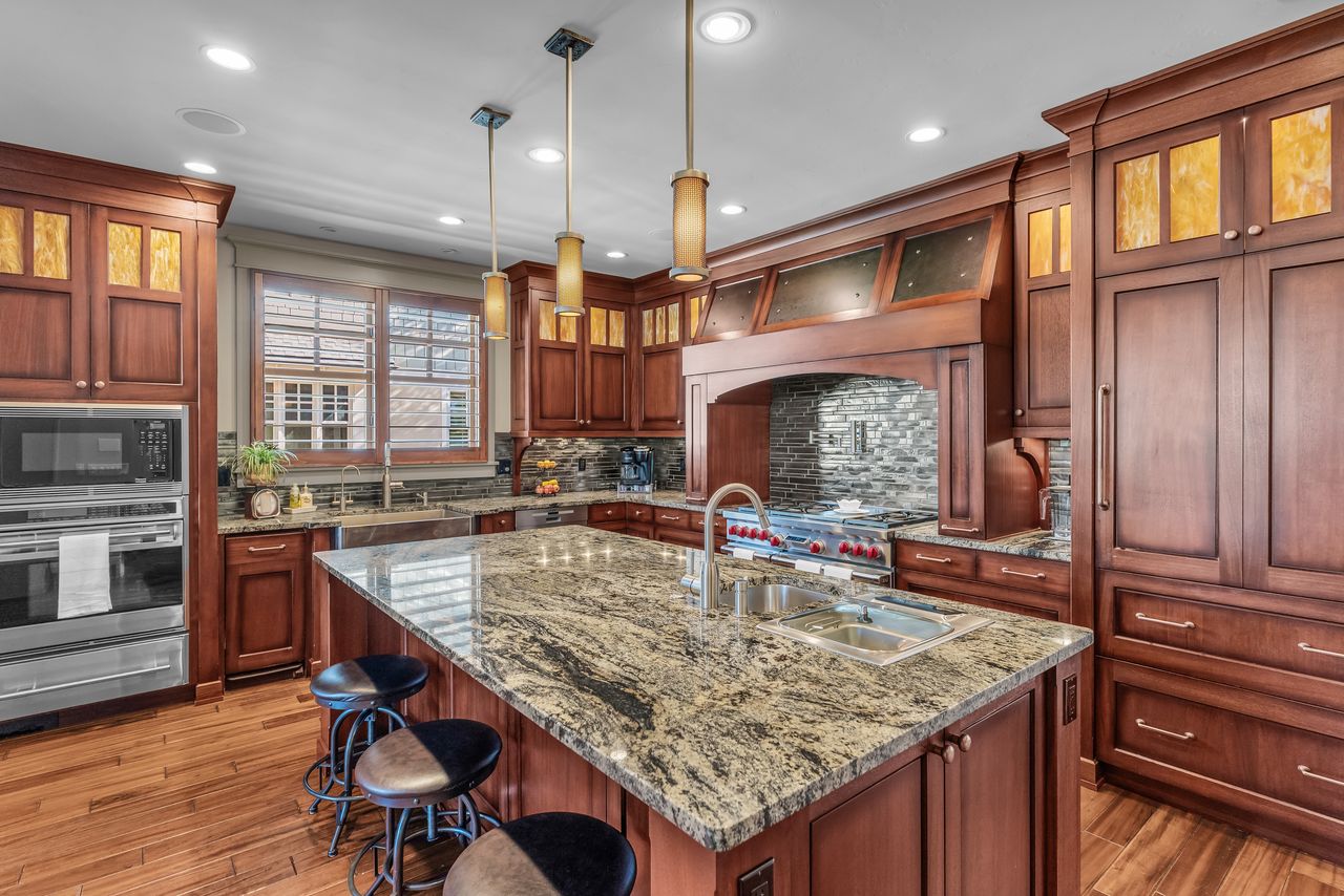 Kitchen featuring light stone countertops, stainless steel appliances, a breakfast bar area, an island with sink, and glass fronted cabinets
