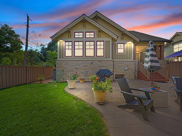 Back of house at dusk featuring a fenced backyard, a patio area, stone siding, and board and batten siding