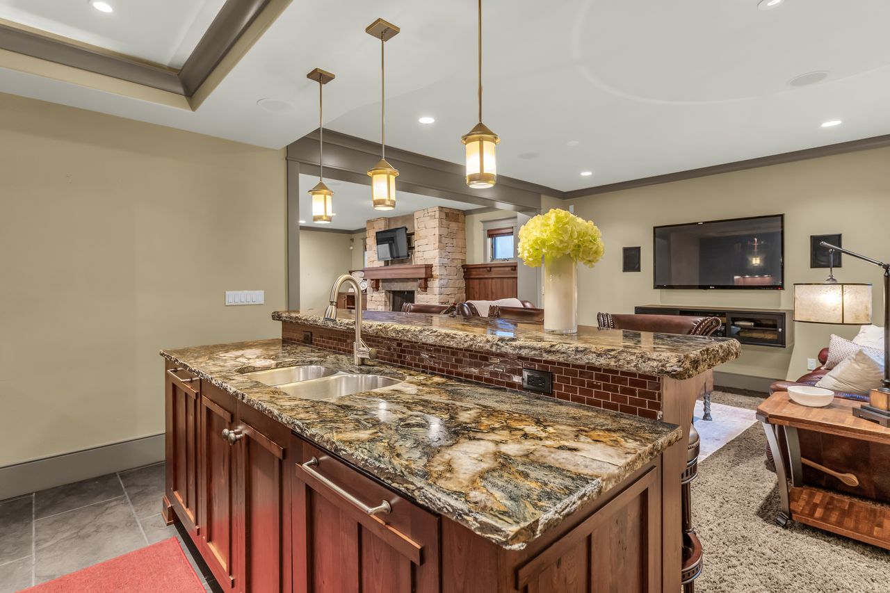Kitchen featuring dark stone countertops, open floor plan, an island with sink, hanging light fixtures, and a fireplace