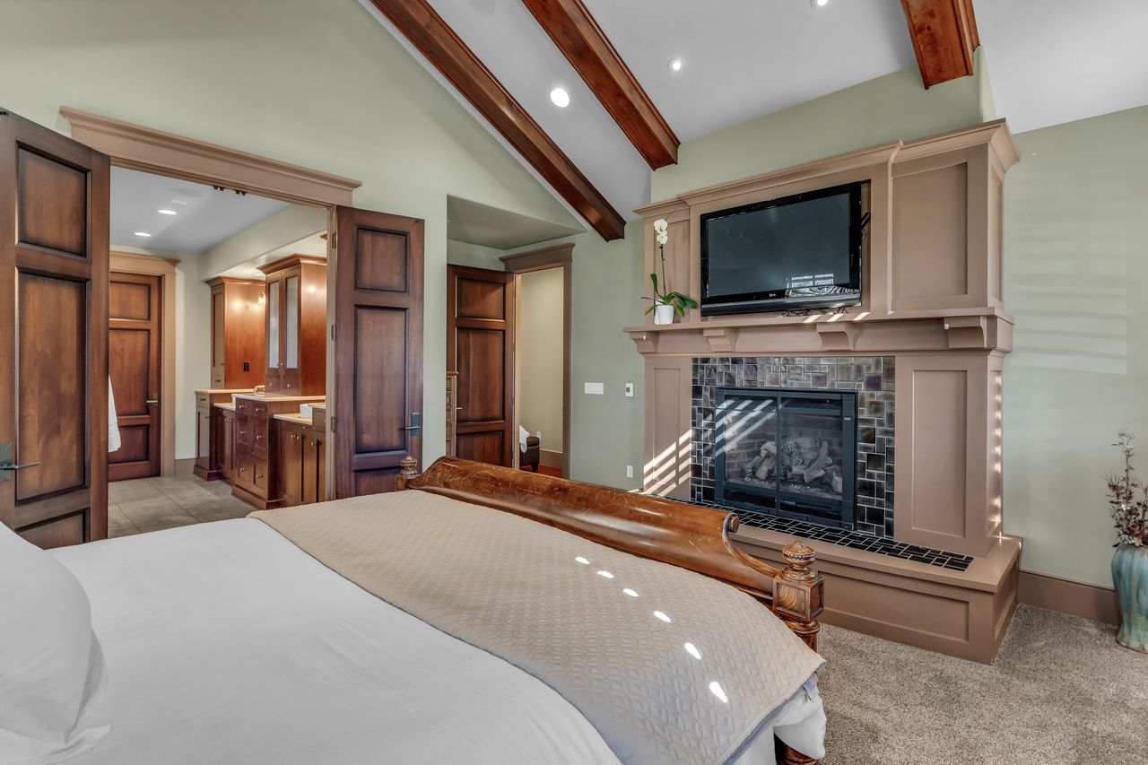 Primary bedroom featuring a tiled fireplace, lofted ceiling with beams, recessed lighting, and light carpet