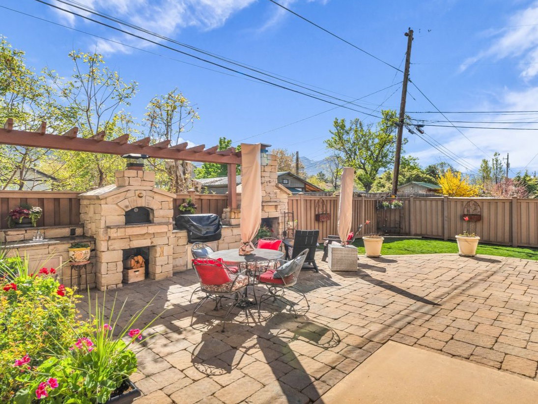 Fenced backyard with an outdoor stone fireplace, a patio area, a pergola, a grill, and outdoor dining area