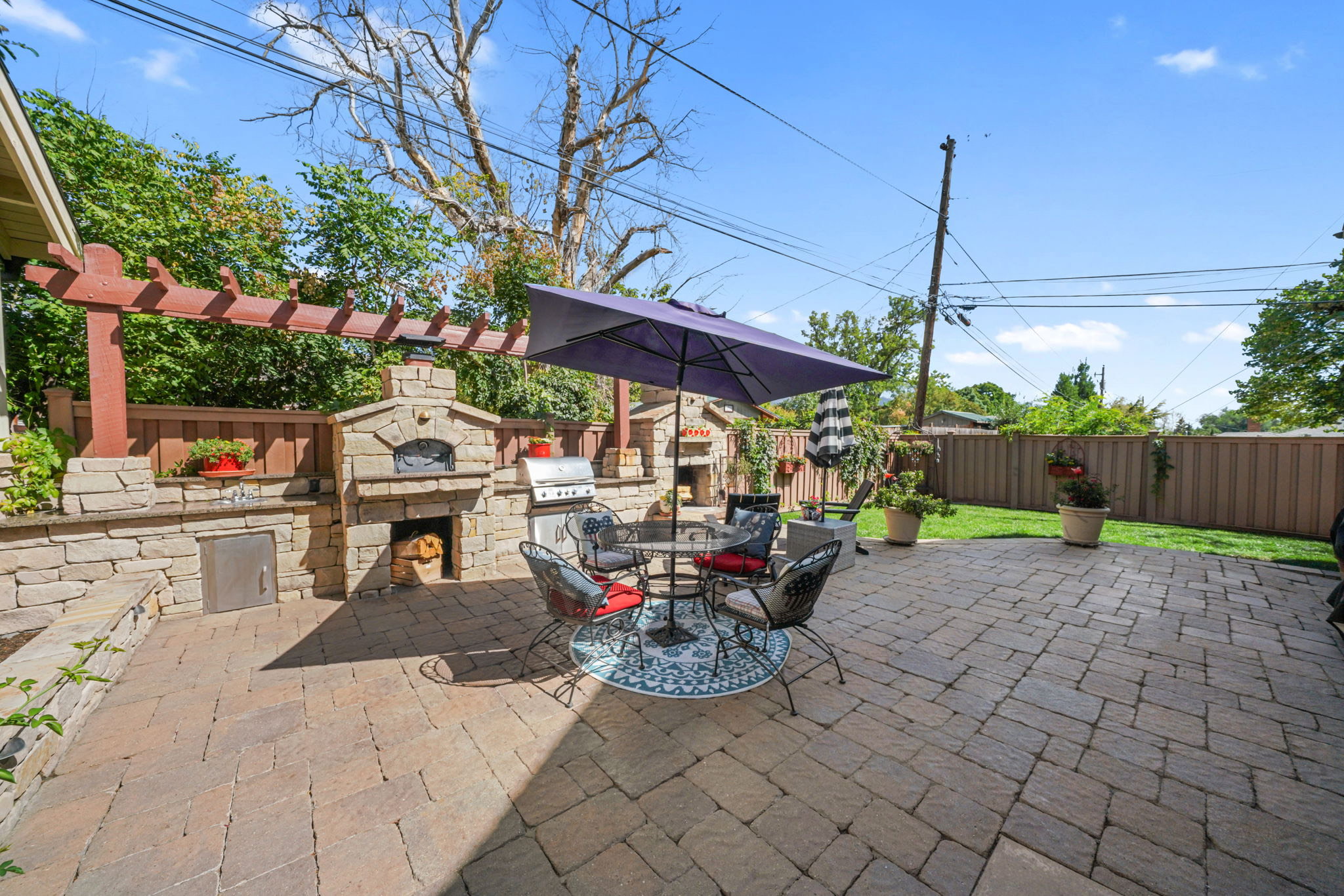 Fenced backyard with an outdoor kitchen / dining area, a patio area, a pergola, and an outdoor stone fireplace