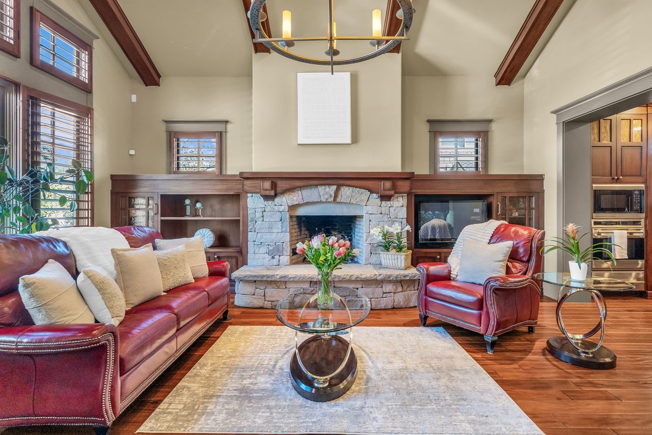Living area featuring a stone fireplace, vaulted ceiling, hanging lights, and wood floors