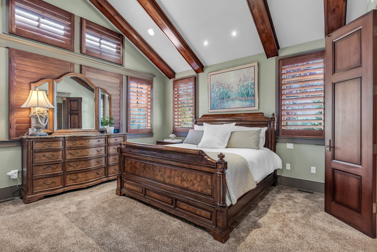 Primary bedroom with light colored carpet, recessed lighting, vaulted ceiling with beams, and multiple windows