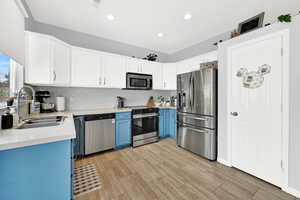 Dual tone kitchen featuring two tone cabinets, stainless steel appliances, light wood-type flooring, decorative backsplash, and light stone countertops