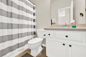 Full bath with curtained shower, vanity, and dark wood-style floors