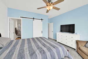 Bedroom with a barn door, light carpet, ensuite bathroom, and a ceiling fan