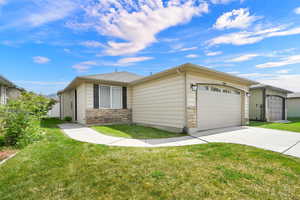 View of front of property featuring stone siding, a garage, concrete driveway, and a front lawn