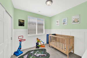 Bedroom featuring a crib, wainscoting, a decorative wall, and light carpet