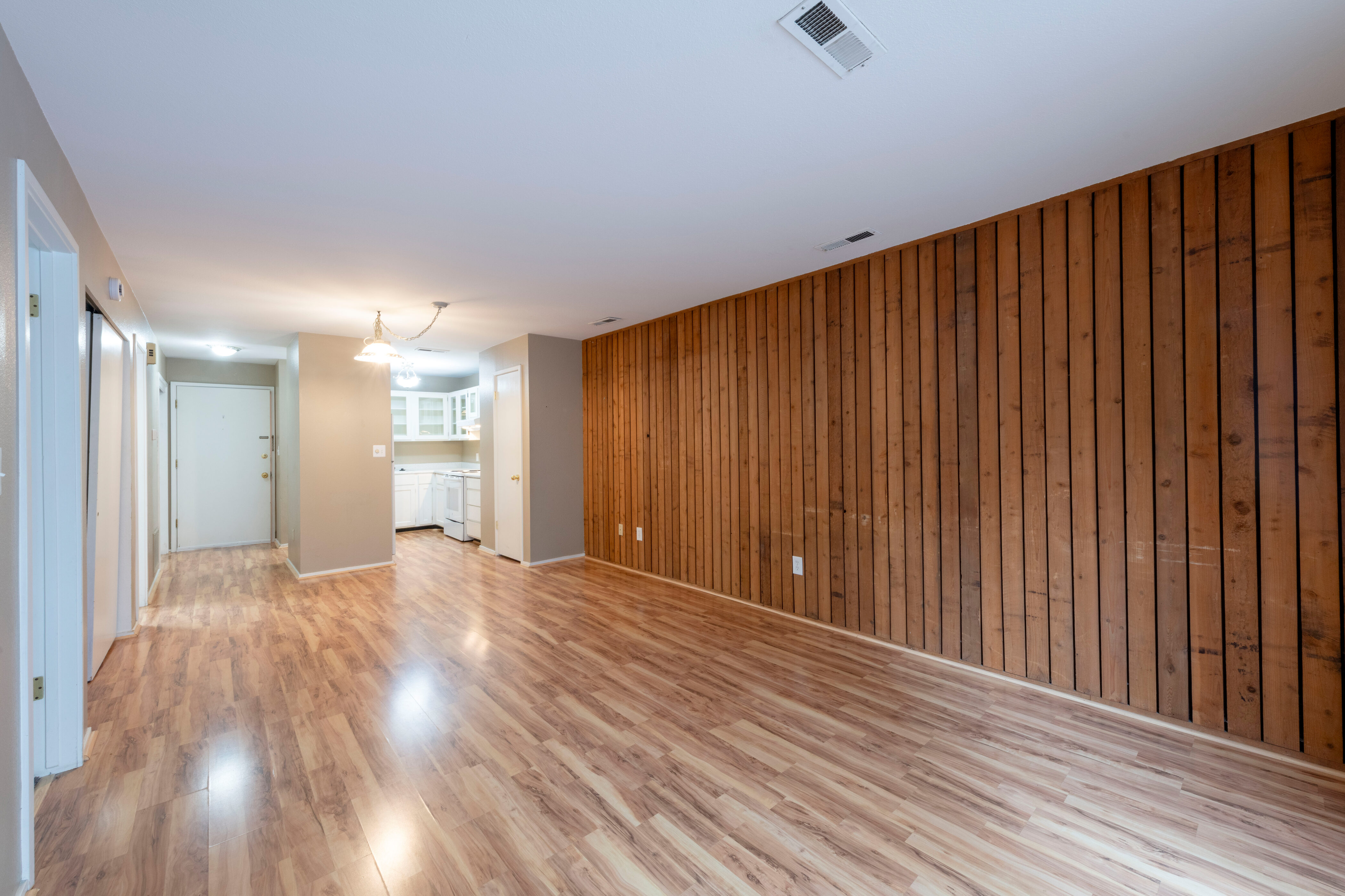 Living area without furniture, light wood-style flooring and wood walls