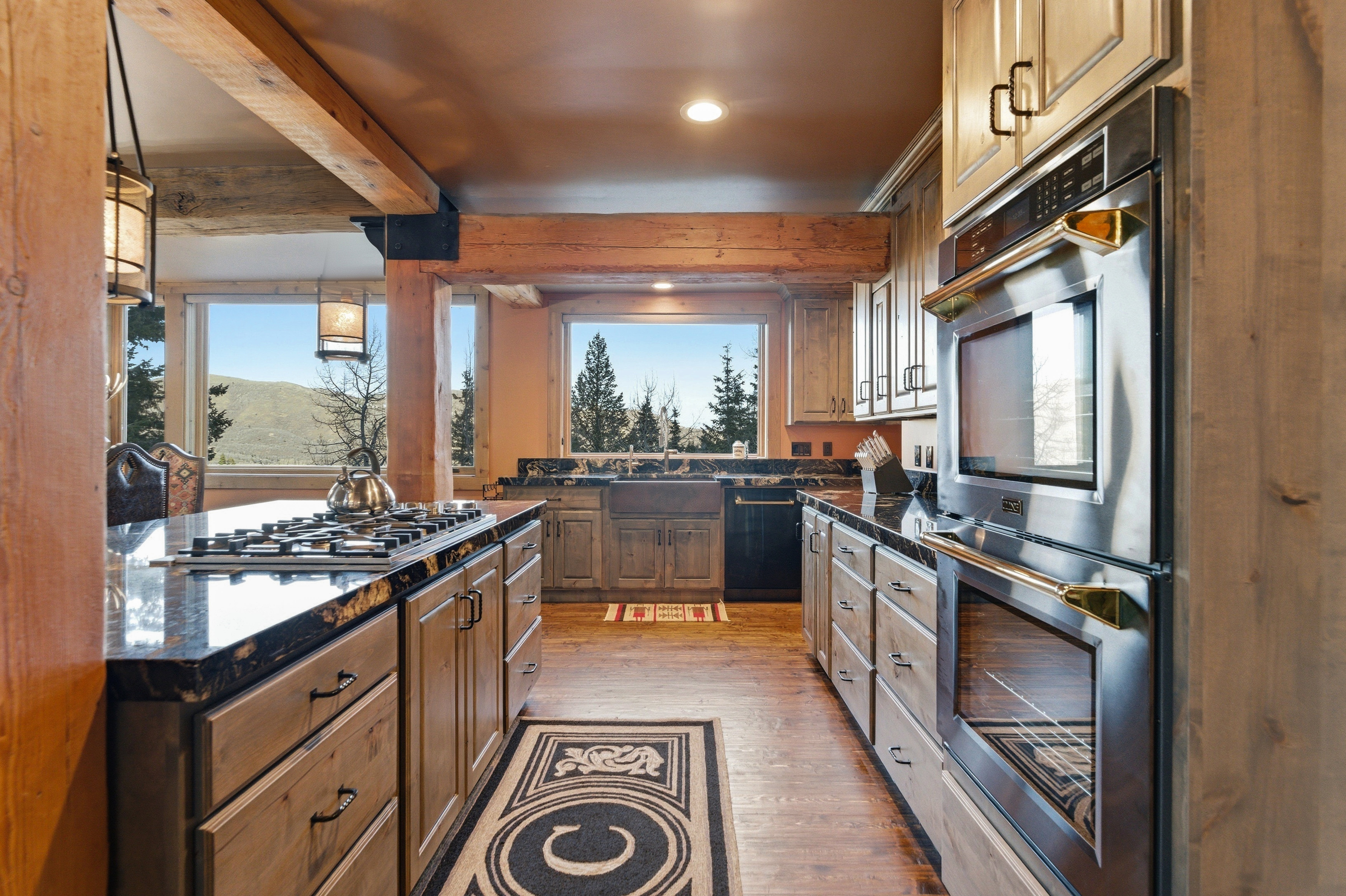 Kitchen with stainless steel appliances, light wood-style floors, dark stone counters, pendant lighting, and wood finish cabinetry