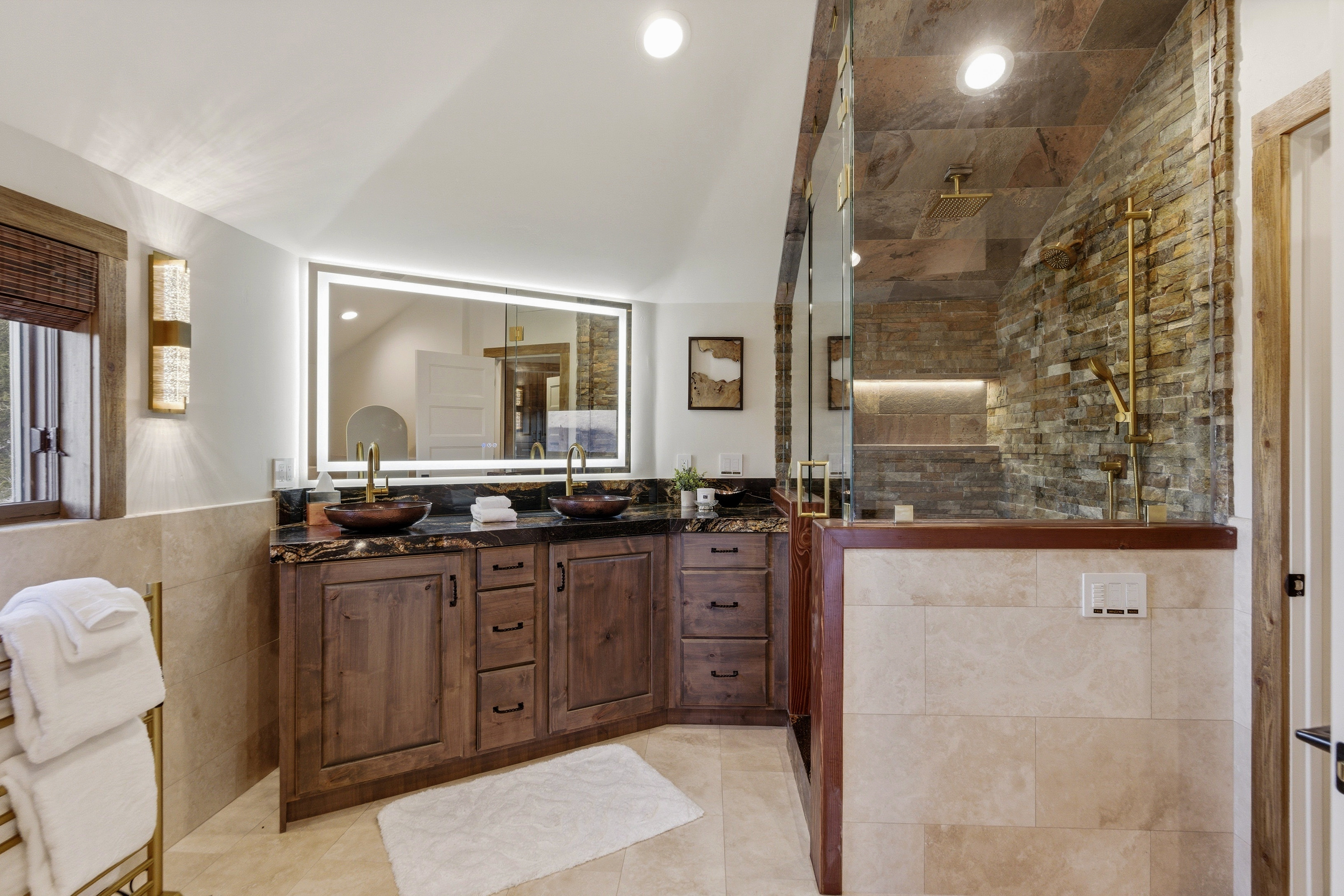 Bathroom with tile walls, a shower stall, double vanity, light tile patterned flooring, and vaulted ceiling