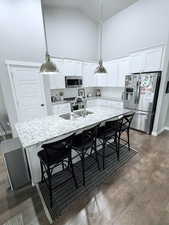 Kitchen with pendant lighting, stainless steel appliances, light stone countertops, a kitchen breakfast bar, and lofted ceiling