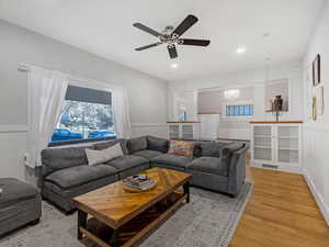 Living area featuring ceiling fan, a wainscoted wall, wood floors.