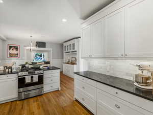 Kitchen with gas stove, a wainscoted wall, wood flooring, white cabinetry, and decorative light fixtures