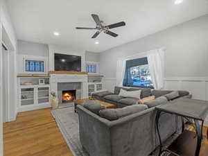 Living area with a fireplace, a wainscoted wall, a ceiling fan, wood floors, and recessed lighting