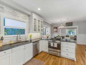 Kitchen featuring a peninsula, stainless steel appliances, white cabinets, a wainscoted wall, and wood floors